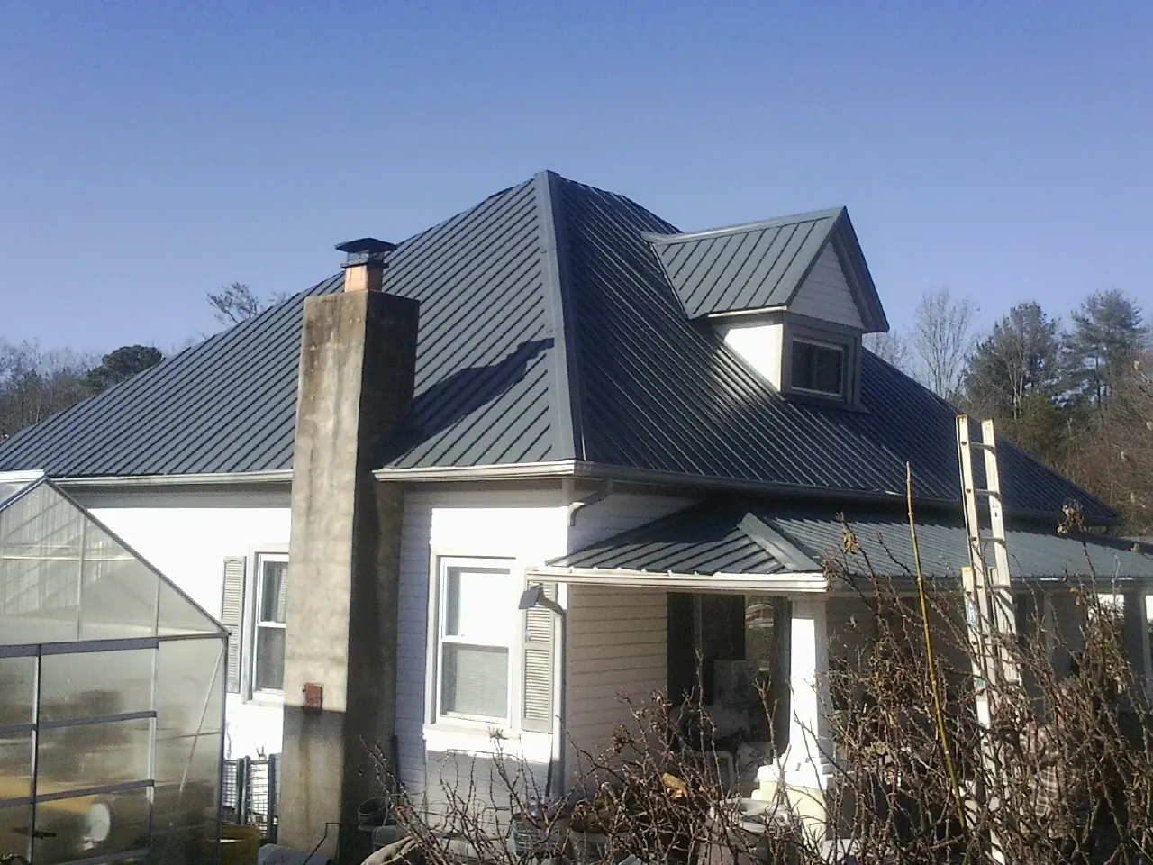 Dark blue standing seam metal roof on a white farmhouse with dormer — Slate & Tile Roof Repair by Roofing Brothers in Cropwell