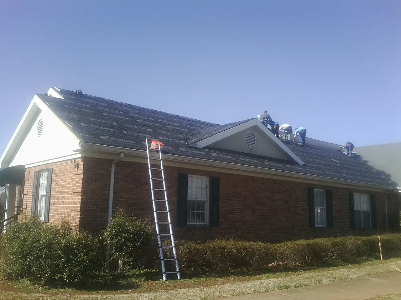Crew tearing shingles off a brick ranch roof with a ladder set — Metal Roof Repair work by our crew in Cropwell