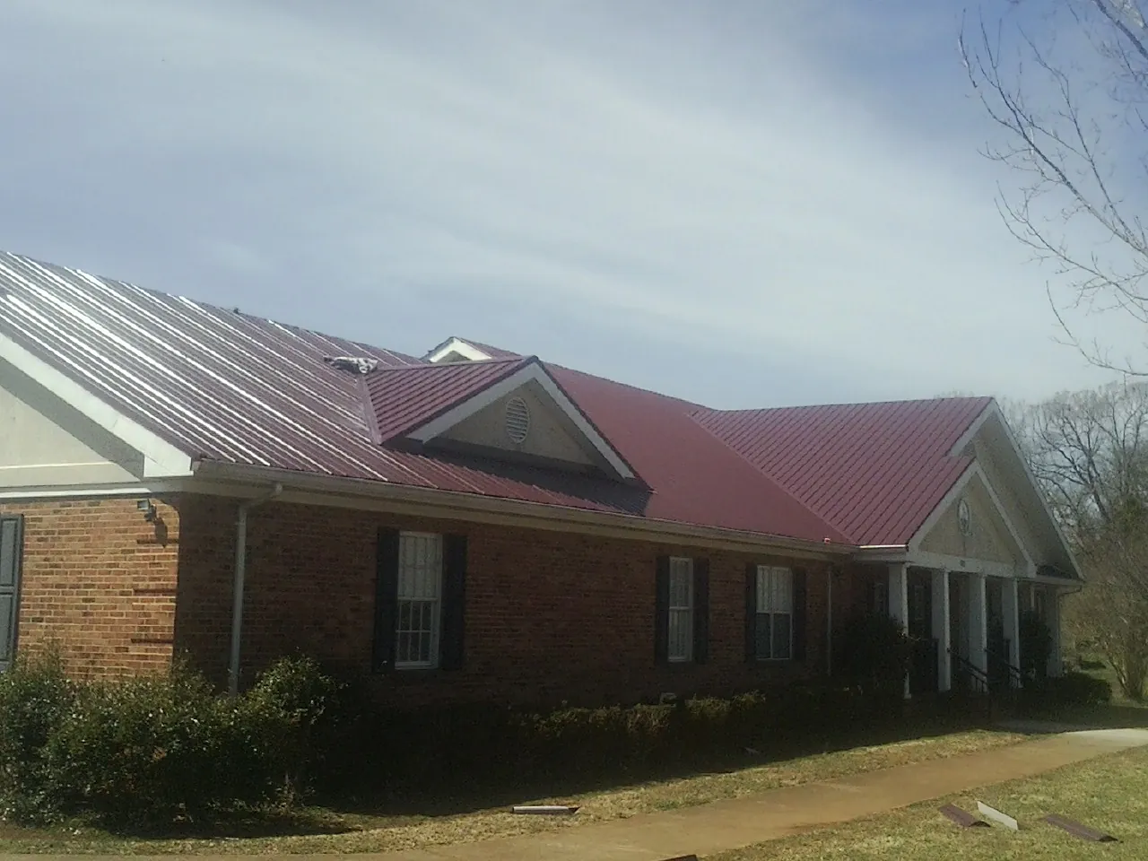 Red metal roof with gabled entries on a long brick building, from a Hail Damage Roof Repair job in Cropwell