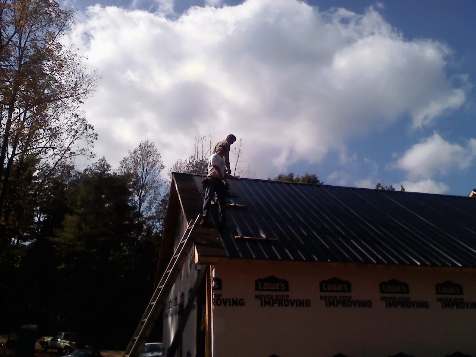 Roofer fastening dark metal panels high against a cloudy sky, from a Roof Inspection job in Cropwell