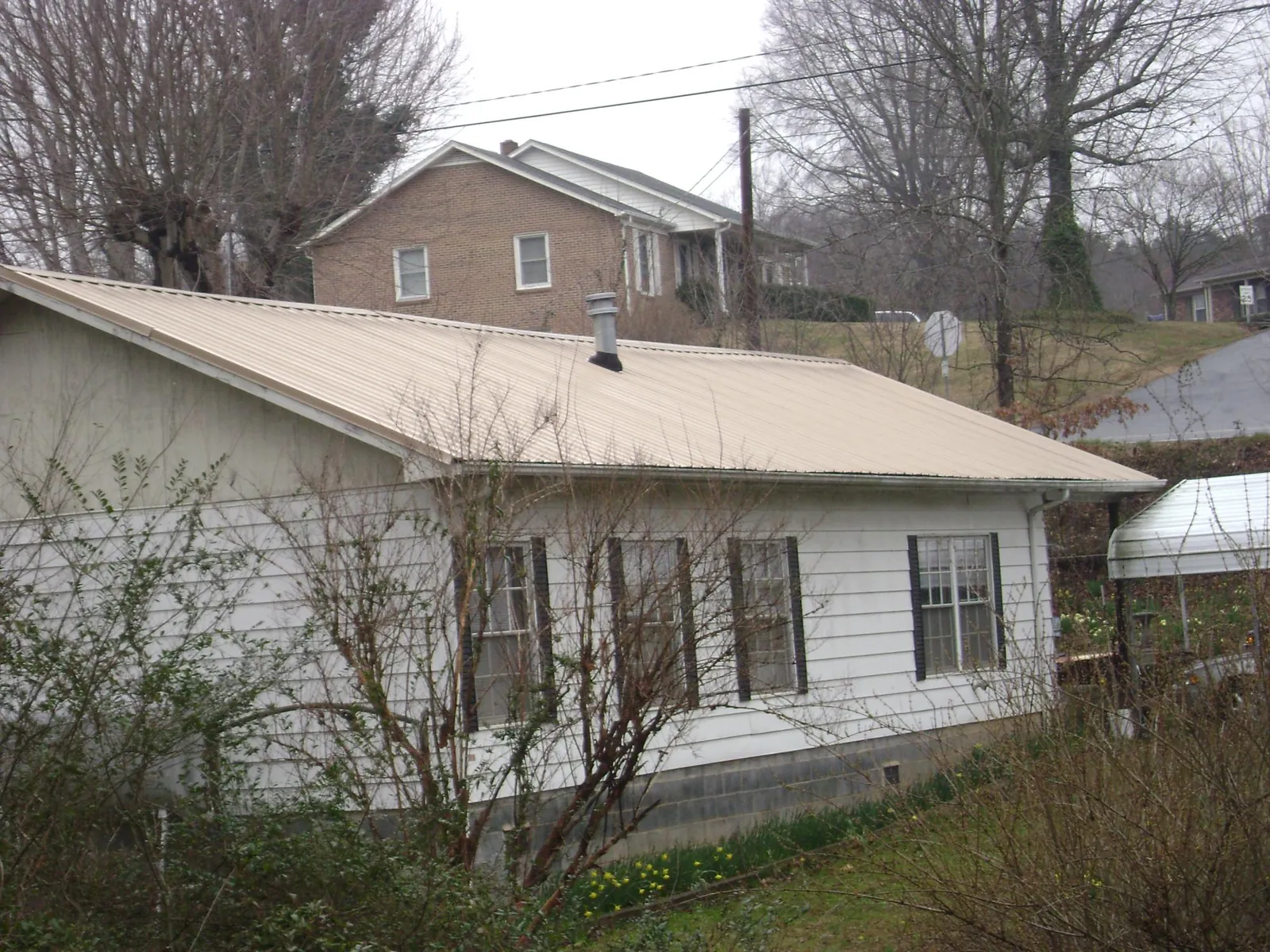 Tan metal roof on a white sided house set into a hillside — Commercial Roofing by Roofing Brothers in Cropwell
