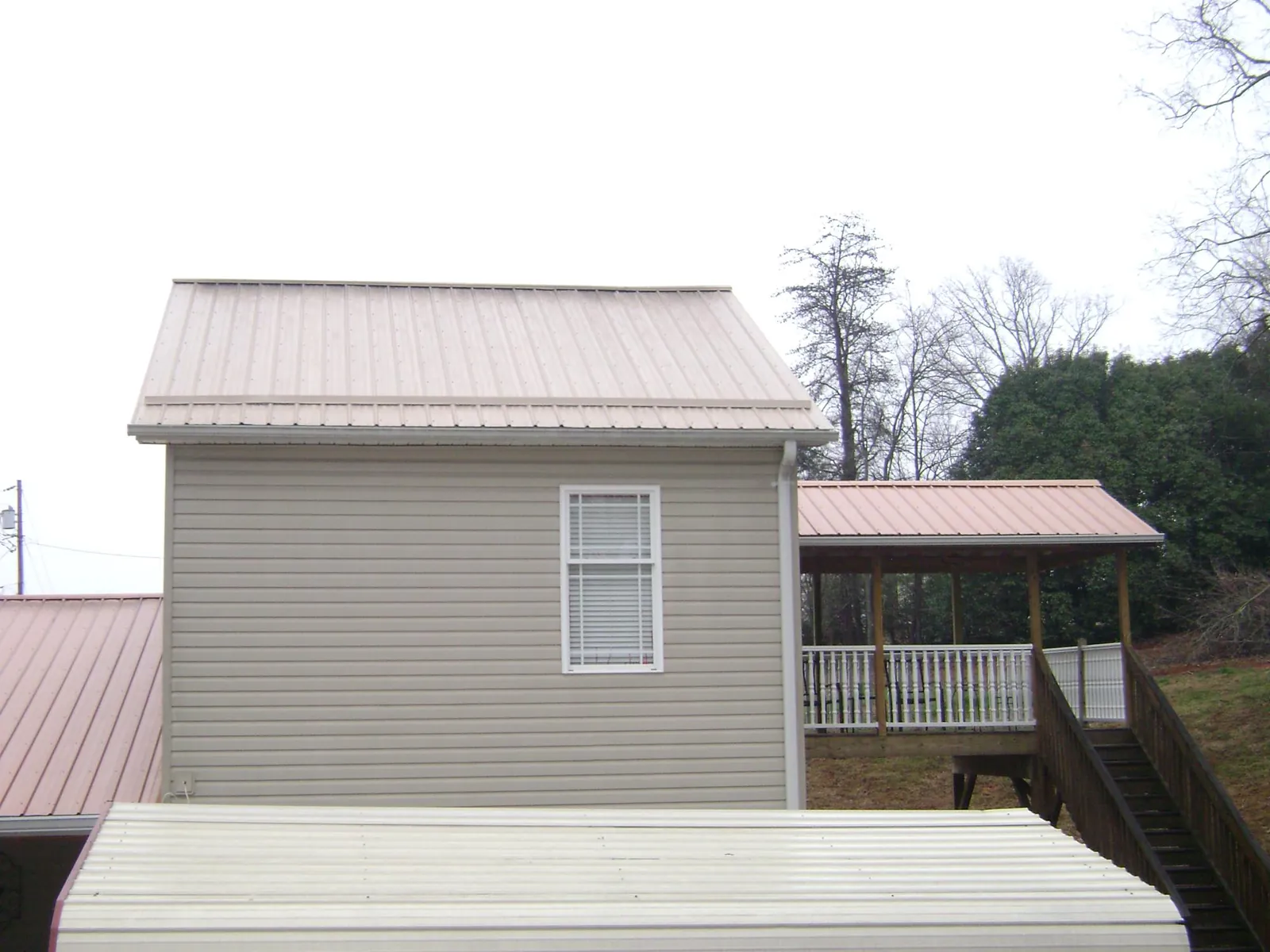 Tan metal roofs on a two story addition and attached porch, from a Roof Replacement job in Cropwell